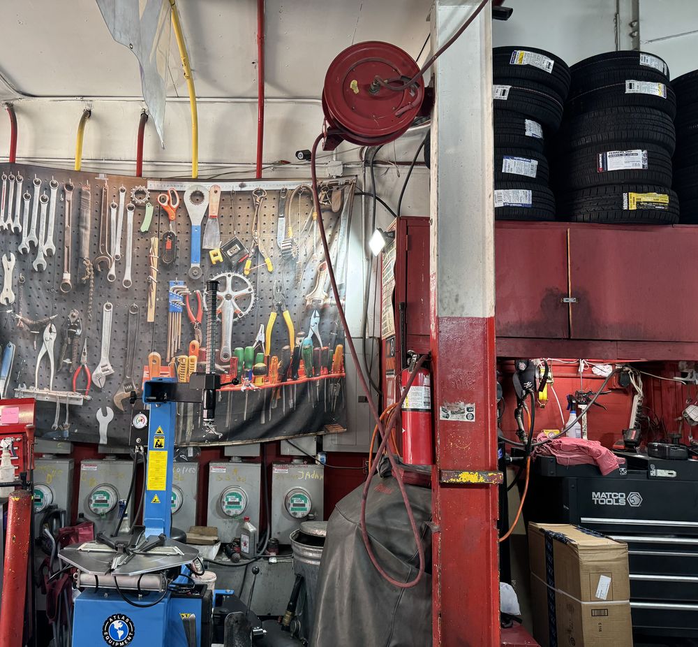 The tool wall at GR Auto Center: wrenches and pliers hung on a pegboard beside a tire changer, with new tires stacked on red racks above.